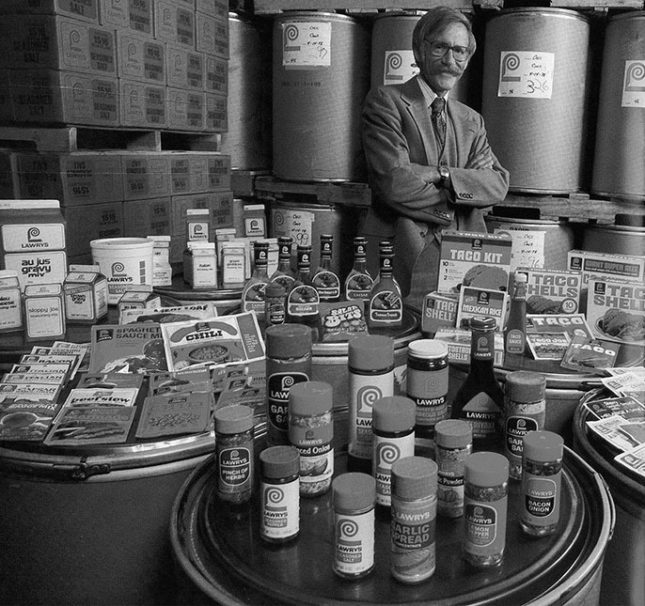 Black-and-white photo of Richard Frank standing proudly behind a display of Lawry's products.