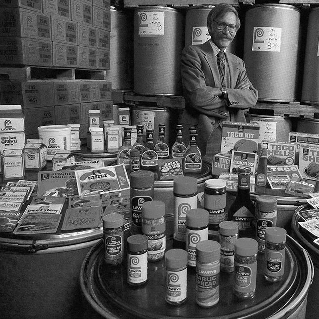 Black-and-white photo of Richard Frank standing proudly behind a display of Lawry's products.
