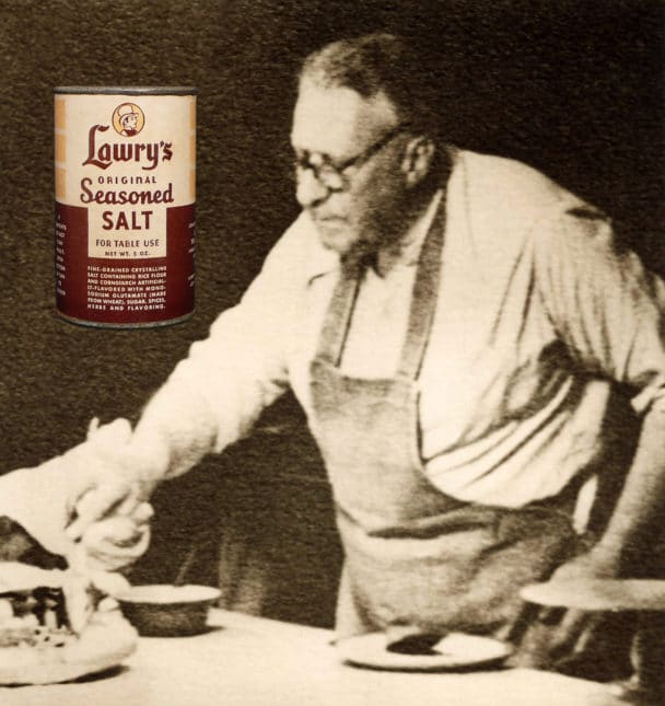 Vintage photo of Lawrence Frank in a kitchen apron poring over bowls of seasonings.