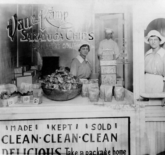 A vintage photo of two women in old-time clothing, seen through a shop window.