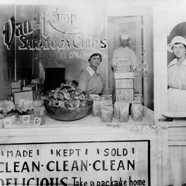 A vintage photo of two women in old-time clothing, seen through a shop window.