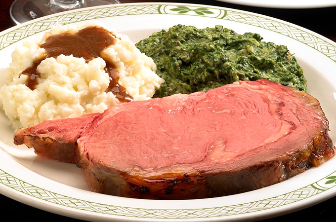 a plate of rare prime rib with mashed potatoes, gravy, and creamed spinnach