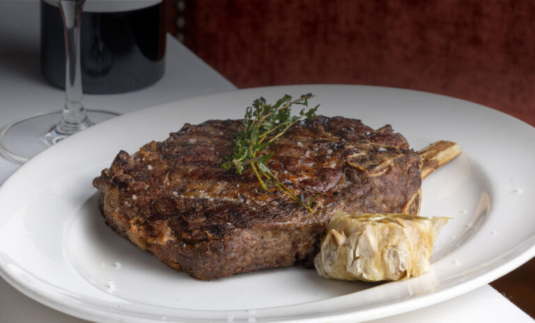 delicious ribeye steak served with garlic confit and a glass of red wine at Lawry's steakhouse who only serves certified Angus Beef brand.